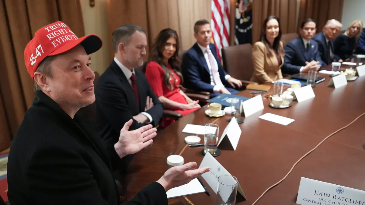 Man in red hat with a ball cap reading "Trump is right about everything" seated at a table with other men and women.