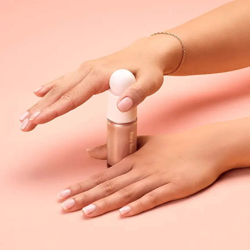 A person using two hands to open Rare Beauty's Positive Light liquid luminizer.