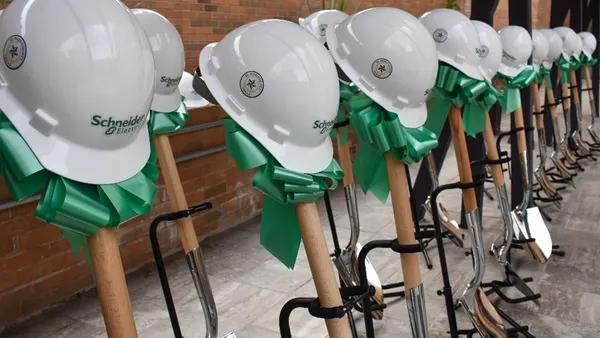 Row of white hard hats with green ribbons placed on shovels for a groundbreaking ceremony.