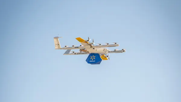 A drone in the sky carries a Walmart-branded package.
